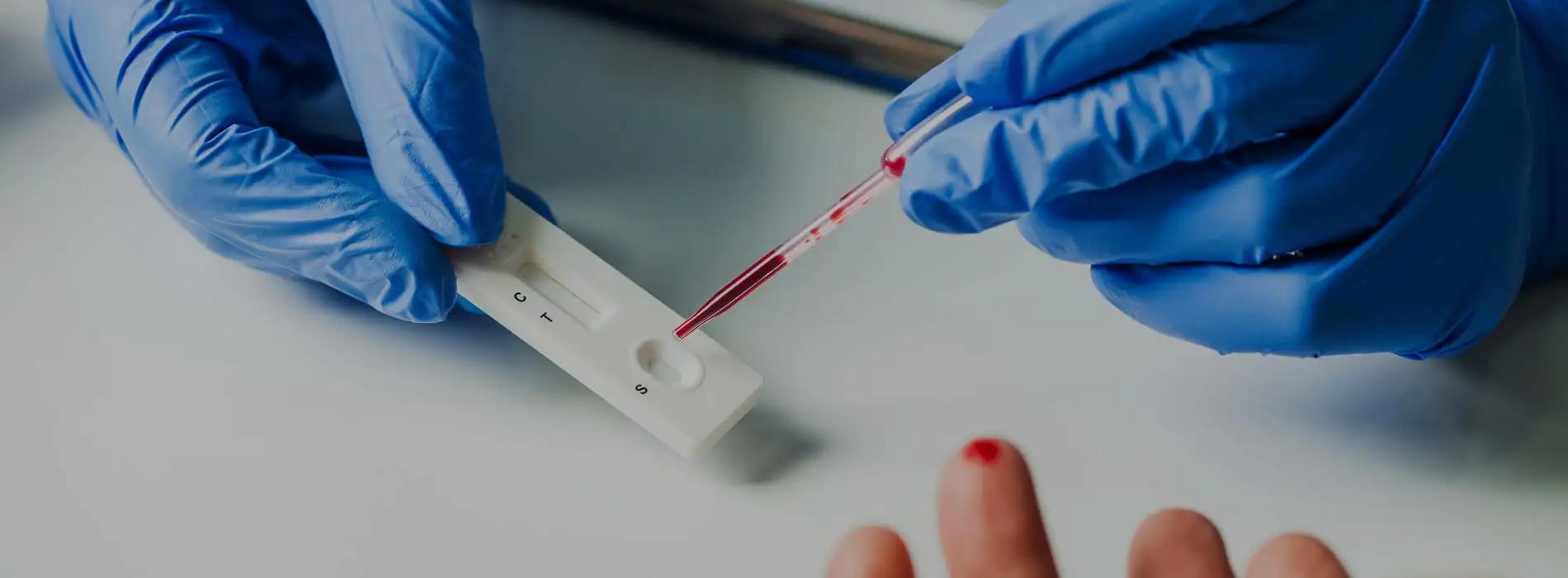 Osoba w rękawiczkach pobierająca krew od pacjenta i wykonująca test antygenowy